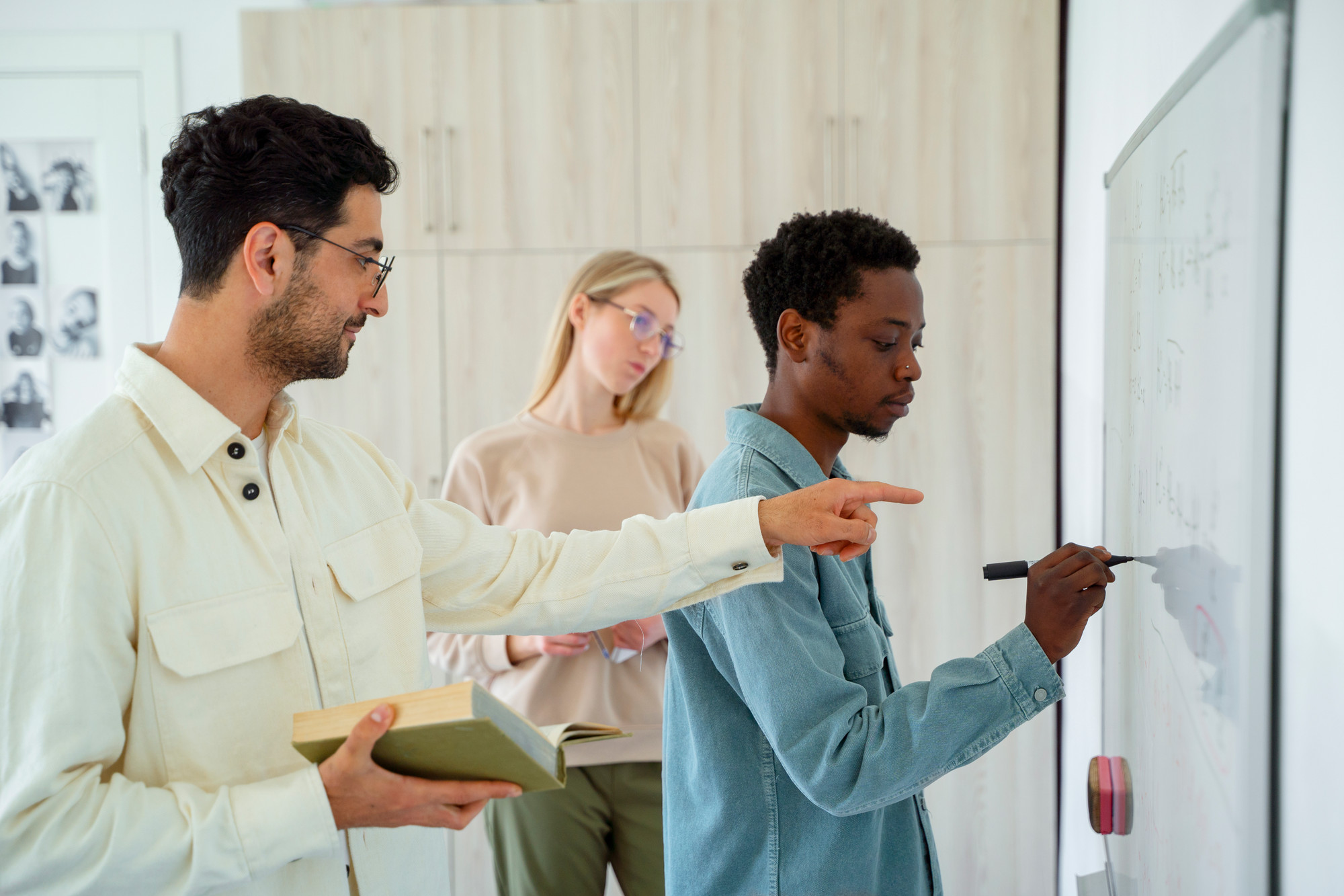 A group of three young people work at a whiteboard. .