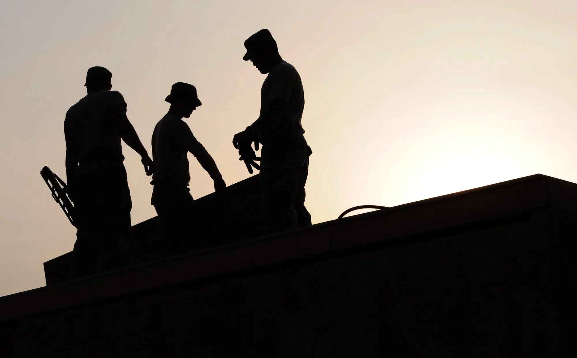 3 male figures working against the sun set or sun rise on a construction site.