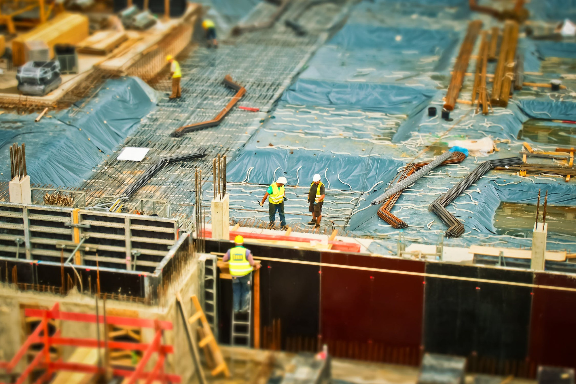 An image from above; three workman work on the roof of a building covered in taupe. One is on a ladder broaching the roof.