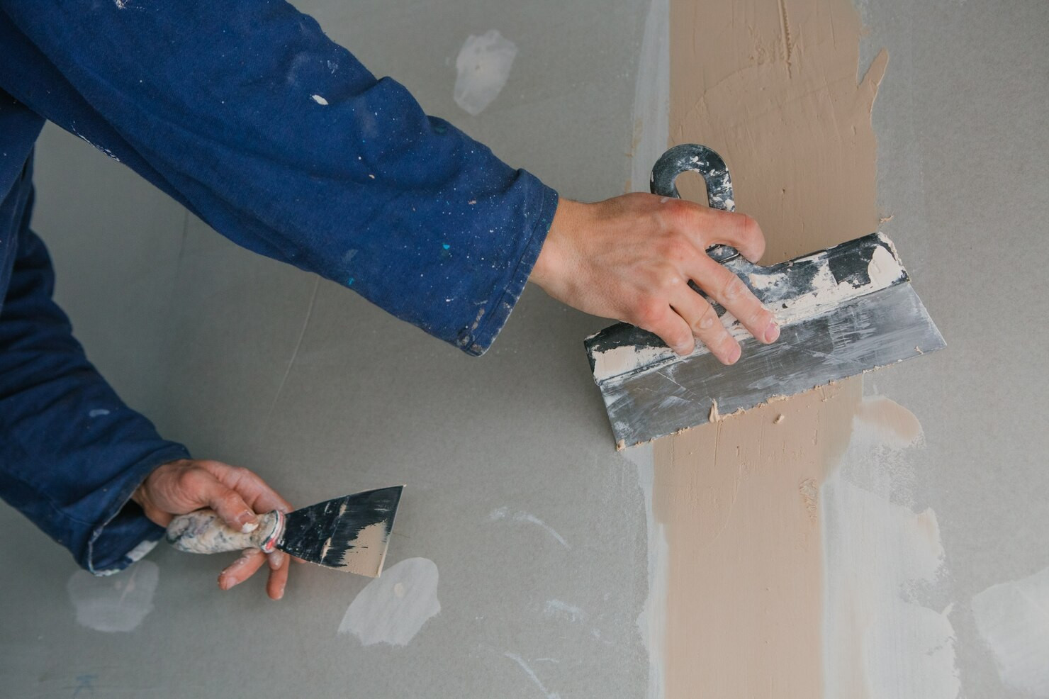 A pair of hands in overalls plasters a wall