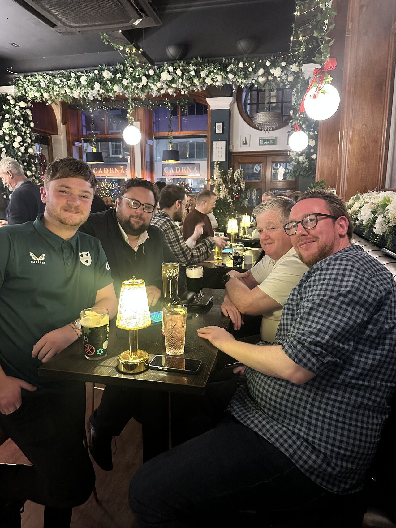 A group of 4 men smile for the camera in the booth of a pub at Christmas time