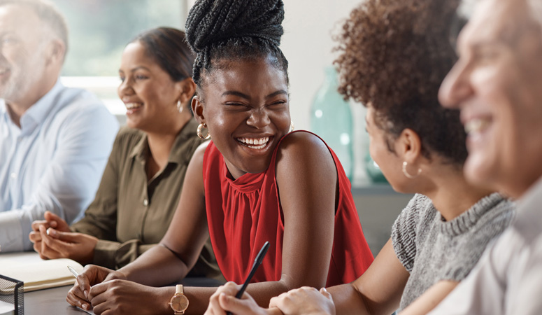 A woman smiles widely at her colleague in a meeting.