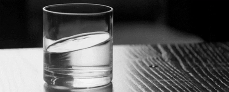 A glass of water on a wooden surface. The water appears tilted.