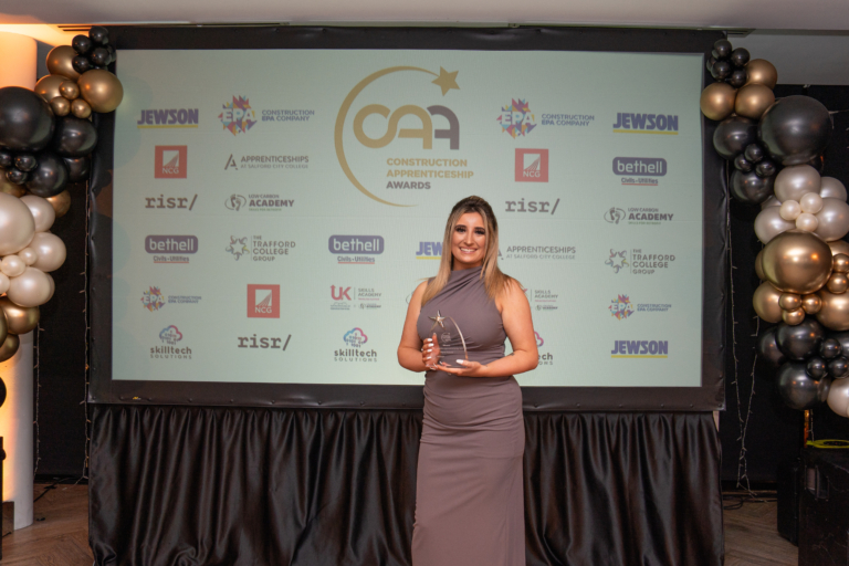 Alyssa Howard poses with an award in formal wear in front of a display of industry logos