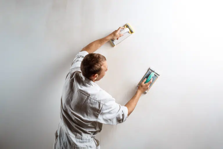 A male in white overalls plasters a wall