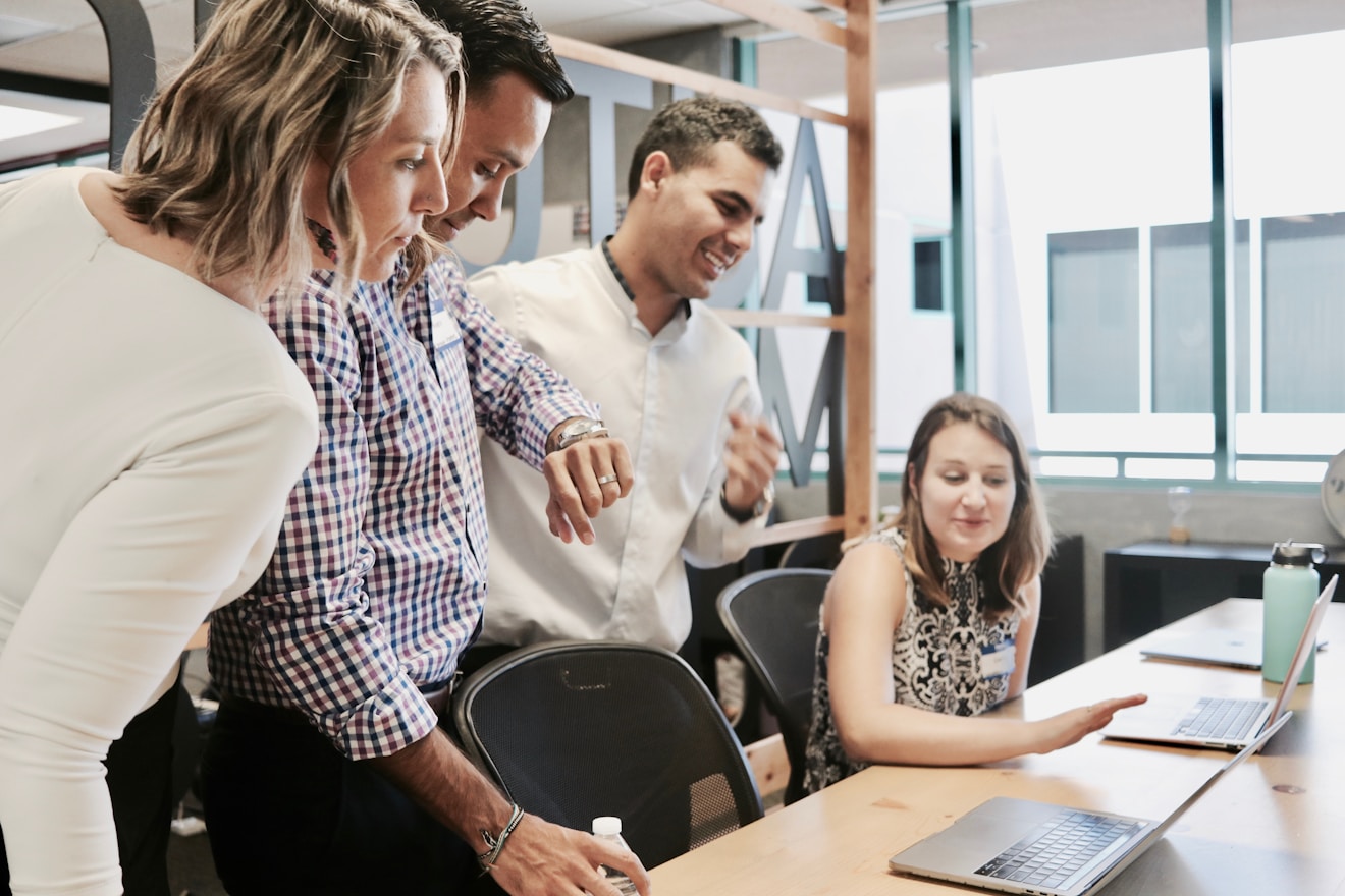 A group of colleagues gather around a laptop and have a discussion in a well-lit office
