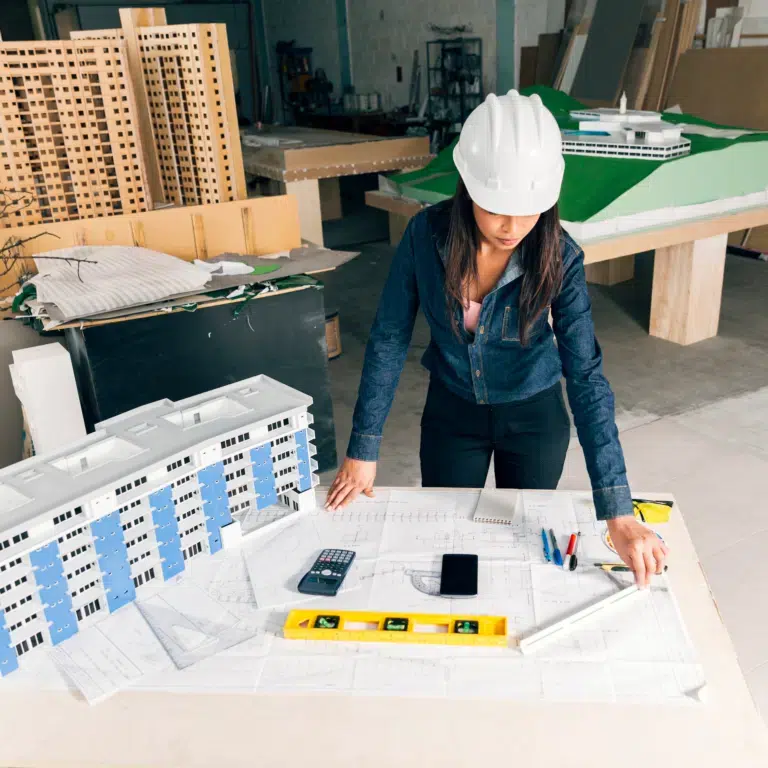 A female construction worker looks over construction plans in a room of models.