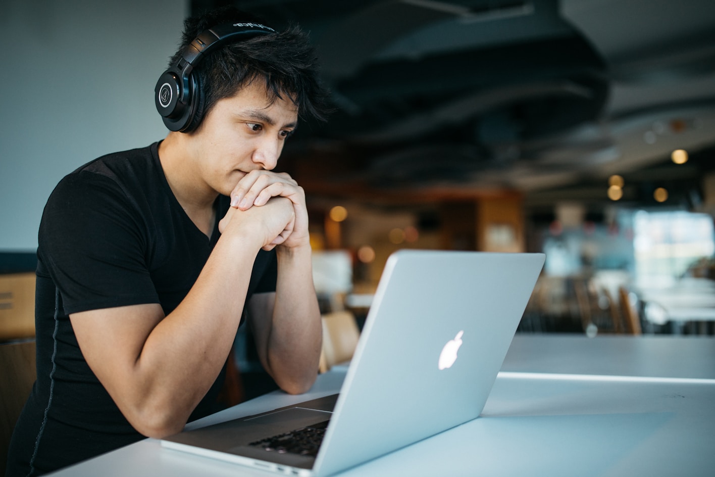 A man rests his chin on his hands as he looks down at a laptop.