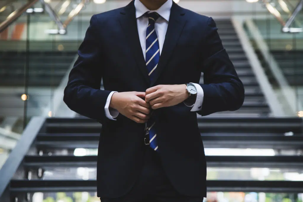 A business man walks down the stairs of a large office and does his suit jacket button up.