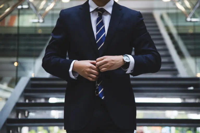 A business man walks down the stairs of a large office and does his suit jacket button up.