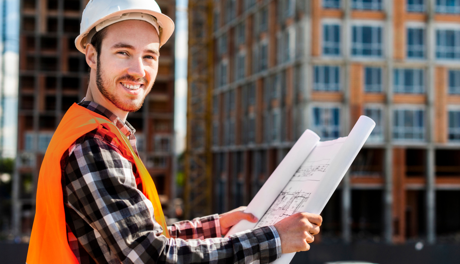 A man wearing a hard hat holds construction plans. He smiles