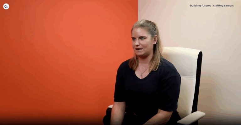 Charlotte Farmery sits in an office chair talking against an orange background